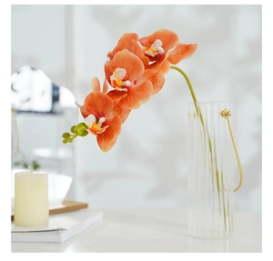 Close-up of orange artificial orchid in a clear glass vase with a golden handle