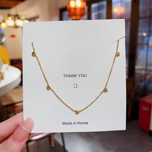Close-up of gold tassel necklace with five small heart pendants on a display card