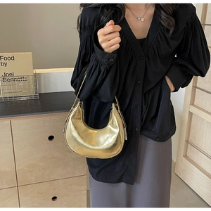 Close-up of a metallic gold hobo crescent shoulder bag worn with minimalist black outfit