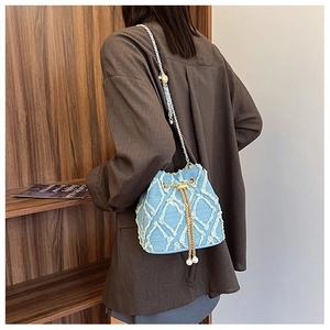 Blue denim bucket bag with diamond tassel pattern and gold chain strap shown on a model