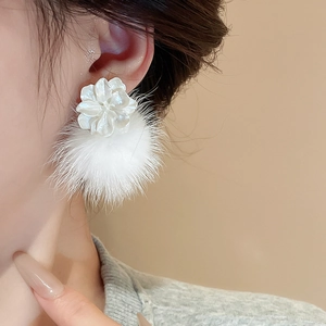 Détail d'une boucle d'oreille fleur blanche avec pompon doux pour l'automne et l'hiver