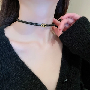 Close-up of black braided leather choker featuring a gold interlocking letter metal buckle
