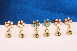 Detail of colorful flower stud earrings with hanging gold balls on a blue background