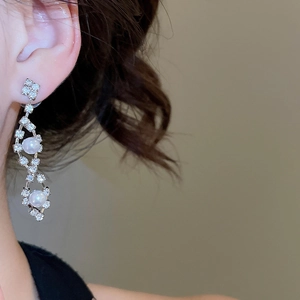 Detailed view of silver flower earrings with clear diamonds and white pearls on model