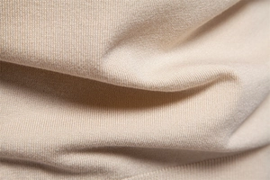 Macro shot of beige knitted fabric showing soft texture and fine stitching detail on polo shirt