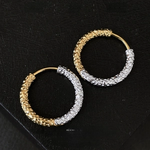 Macro detail of mixed gold and silver earrings with lava texture on black leather