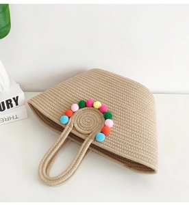 Detail of handmade straw tote bag featuring colorful pom-poms and woven texture