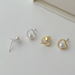 Close-up of twisted heart earrings featuring white pearls in gold and silver finishes