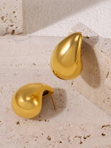 Macro shot of gold teardrop earrings with mirror finish on textured stone background