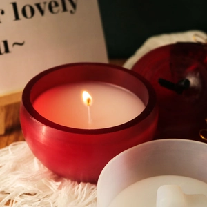 Scène chaleureuse montrant une bougie rouge allumée et un pot blanc en verre dépoli