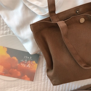 Detail of dark brown canvas tote bag with metal snap button and large outer pocket