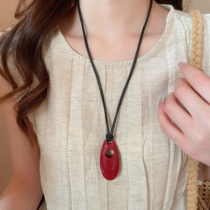 Detail of red geometric oval resin pendant on a black cord worn by a model