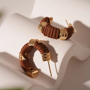 Détail macro de boucles d'oreilles géométriques en C avec cuir tressé marron et fini doré