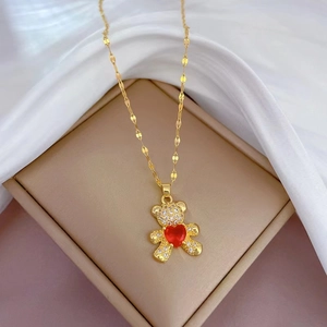 Detail of gold teddy bear pendant with clear zircon and red heart stone on beige jewelry box