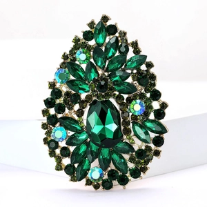 Macro view of a gold-plated brooch featuring emerald green crystals in a leaf design