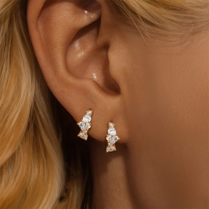Close-up of gold water-drop heart earrings with inlaid crystals on an earlobe