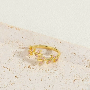 Detailed view of a gold vine ring with pink marquise zircon on a beige stone surface