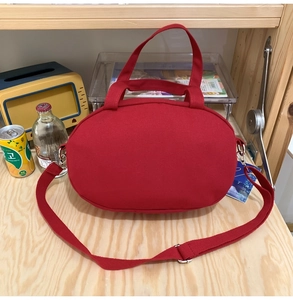 Detail of red oval canvas bag on wooden table with shoulder strap and handles