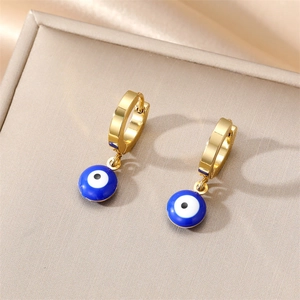 Macro shot of gold evil eye hoop earrings with blue enamel charms on a beige jewelry box