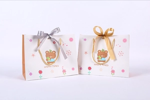 Detail of cartoon bear gift bags with satin bows and golden handles on white paper