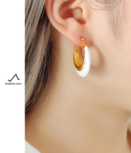 Detail view of gold stainless steel hoop earrings with white enamel on model ear
