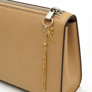 Primo piano della borsa in pelle beige con ciondoli a stella e fiocco dorati sulla zip
