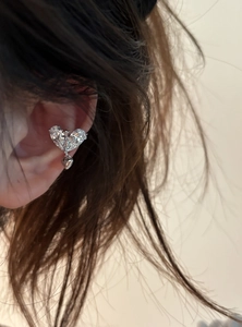Gros plan d'un ear cuff en zircon en forme de cœur argenté avec croix et pendentif