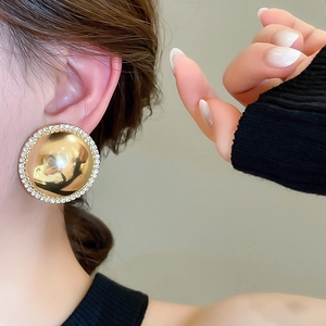 Close-up of model wearing luxury gold round stud earrings with shimmering crystal border