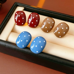 Dettaglio di tre paia di orecchini ovali a pois in resina nei colori rosso, marrone e blu