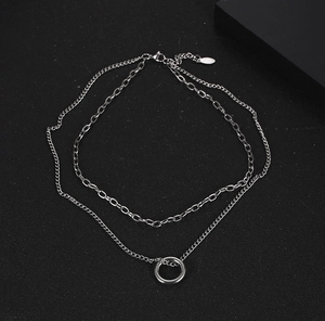Close-up of double-layer silver chain necklace with ring pendant on black background