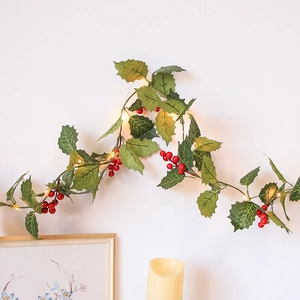 Artificial Christmas garland with red berries and warm LED lights on a white wall decor