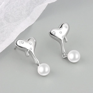 Macro shot of silver lava textured heart earrings with zircons and white pearl drops