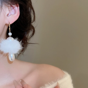 Close-up of elegant gold earrings with white fur pom pom and pearl on female model