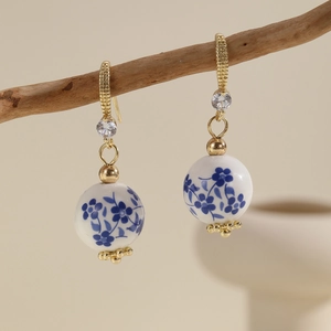 Detailed view of porcelain beads earrings with floral patterns hanging on a branch