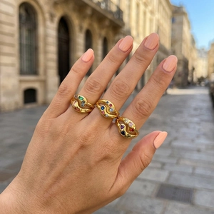Close-up of three gold rings with colorful zircons worn in a stylish outdoor setting