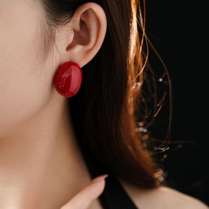 Close-up of a minimalist bright red oval stud earring with glossy enamel finish on model