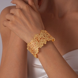 Détail d'un large bracelet manchette doré ajouré avec motif trèfle et fini métallique