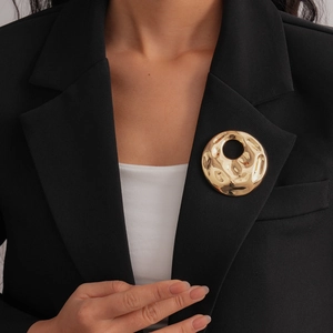 Detail of large gold crumpled round brooch on black suit showing liquid metal texture