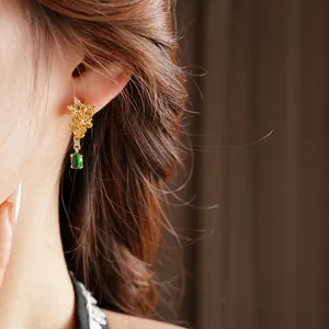Boucles d'oreilles vintage dorées à fleurs avec pendentif en pierre verte sur modèle