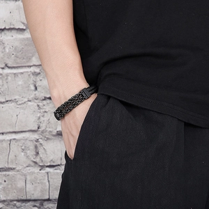 Close-up of men's black leather woven bracelet with textured steel magnetic clasp on wrist
