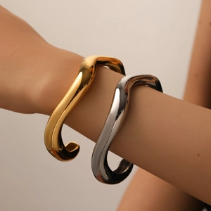 Detail of minimalist wavy stainless steel open bangles in gold and silver finish
