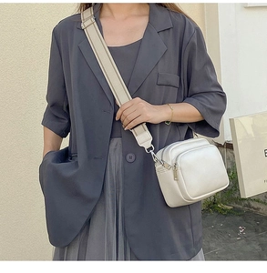 Detailed view of white leather crossbody bag with striped strap on a grey blazer suit