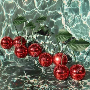 Close-up of red mirror mosaic cherry disco ball with green leaves on a ripple water background