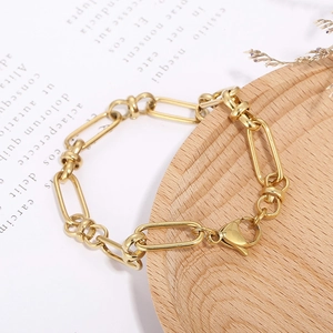 Détail d'un bracelet chaîne en trombone doré sur un plateau de présentation en bois