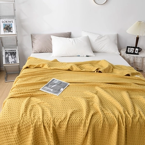 Detailed texture of ginger yellow waffle weave cotton blanket on a white cozy bed