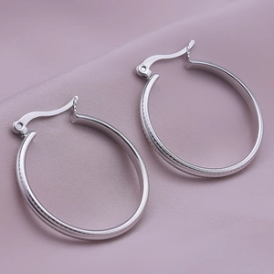 Detailed close-up of silver-tone hoop earrings with textured edges on leather background