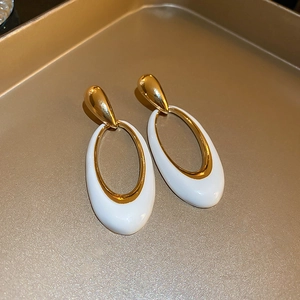 Close-up of golden teardrop studs with white enamel oval pendants on a luxury tray