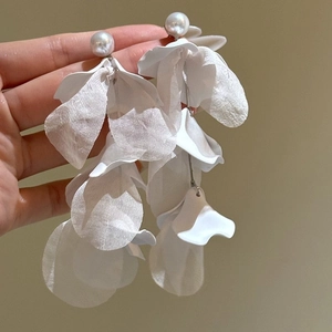 Détail de boucles d'oreilles fleurs en résine blanche avec perles et pompons argentés