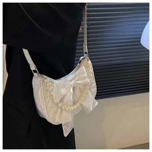Side view of white textured shoulder bag with satin bow and pearl chain on model