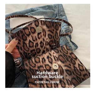 Close-up of leopard print flap bag featuring a metal magnetic buckle and adjustable strap